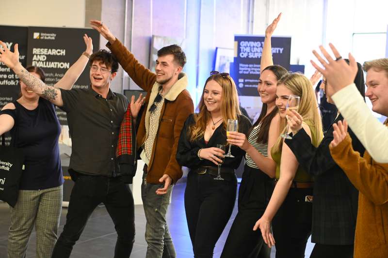 A group of people celebrating at a University of Suffolk Alumni Relations event, smiling and clapping.