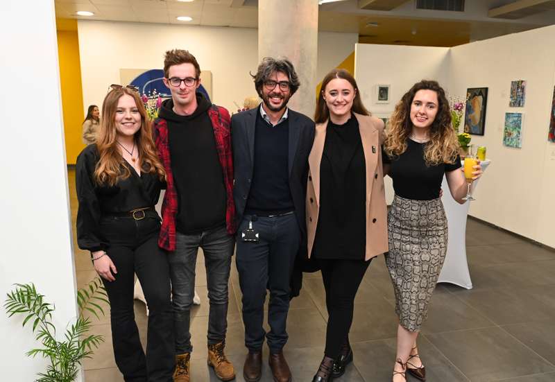 Five people smiling and posing together at an Alumni Relations event, with colorful artwork visible in the background.