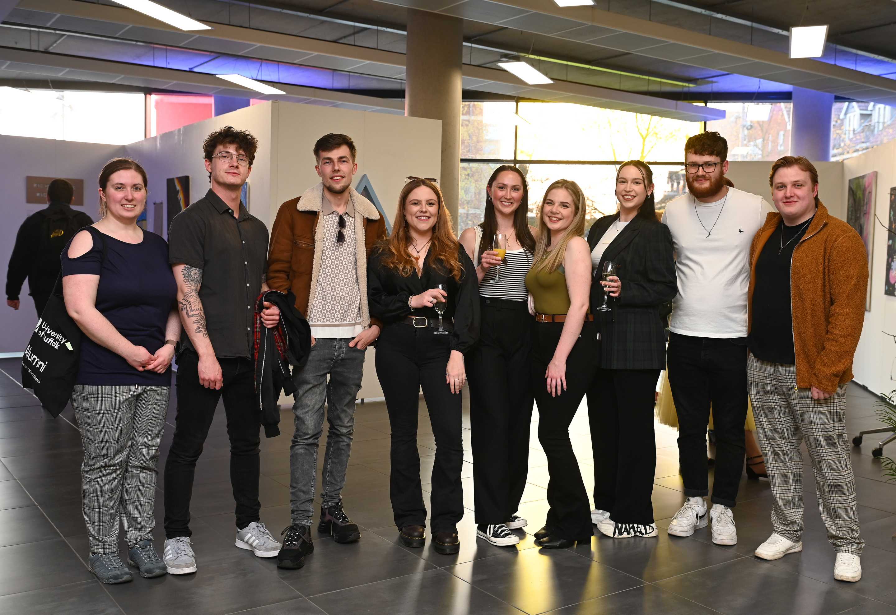 Eight people posing together at an Alumni Relations event, some holding drinks and smiling at the camera.