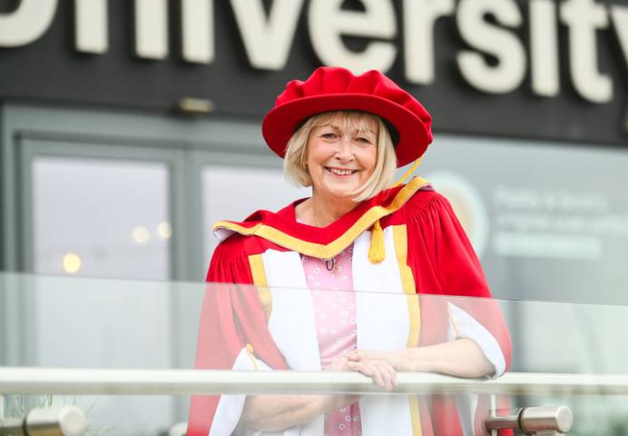 Woman in red and gold honorary graduate robes outside a university building