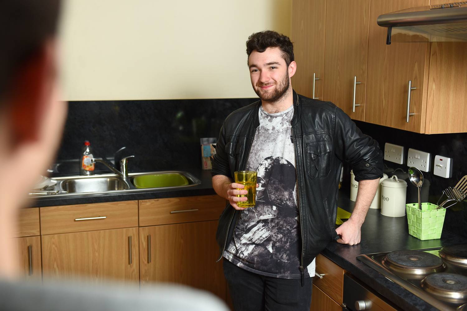 Student standing in a kitchen holding a cup