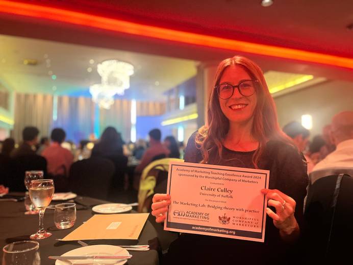 Claire Culley seated at a table at the Academy of Marketing conference awards holding her award and smiling