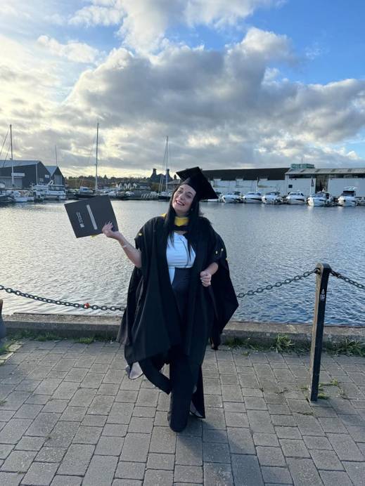 A graduate on the waterfront wearing graduation hat and gown