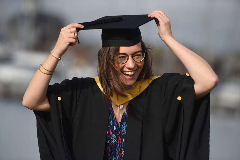A student smiling, holding their mortar board