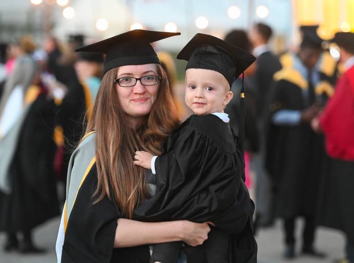 A graduate in a graduation cap and gown holding a child in a matching graduation outfit