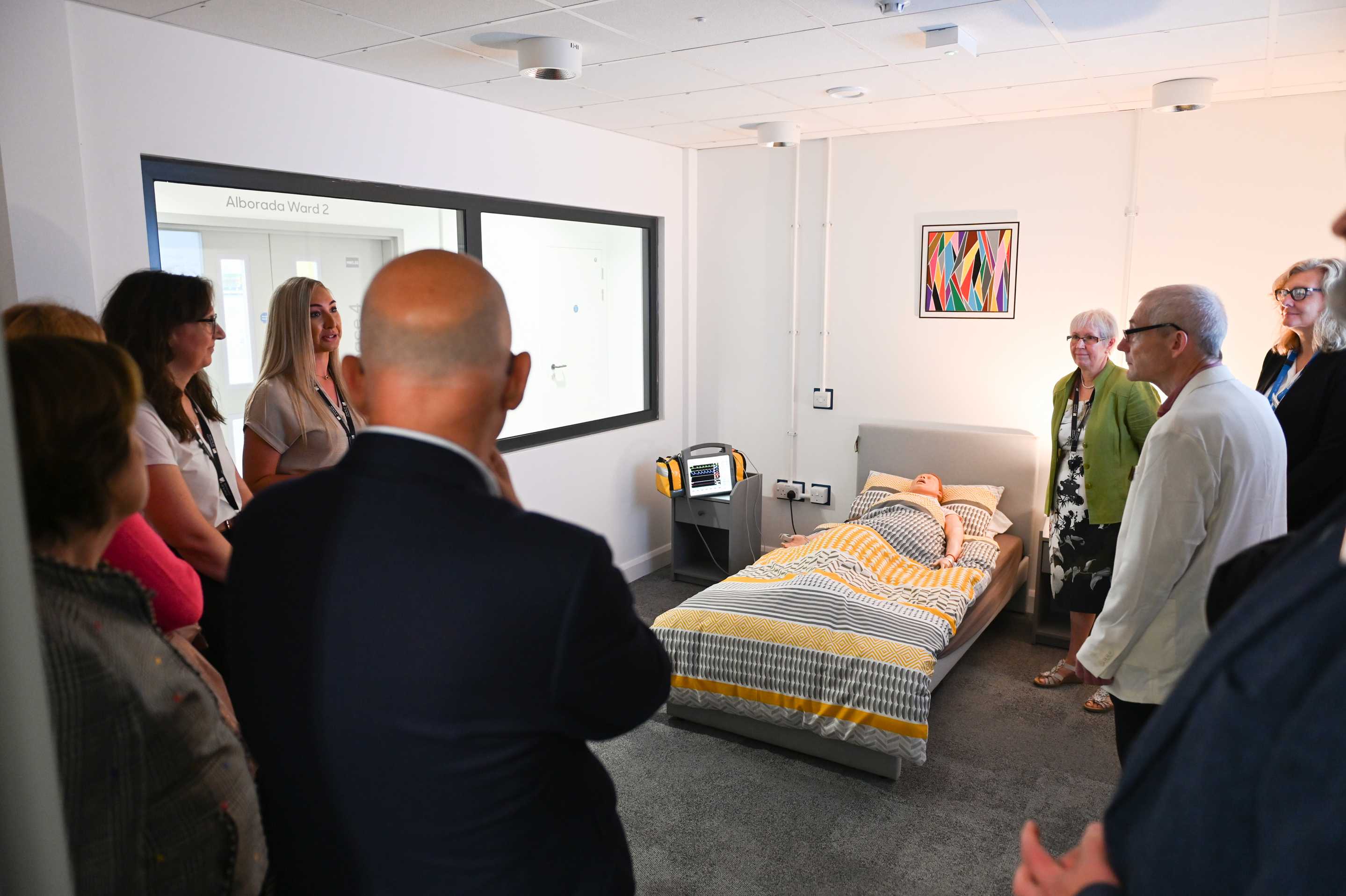 Attendees for the opening of the Health and Wellbeing Building gathered around the bed in the community-flat, as one of the team explains what the space is used for