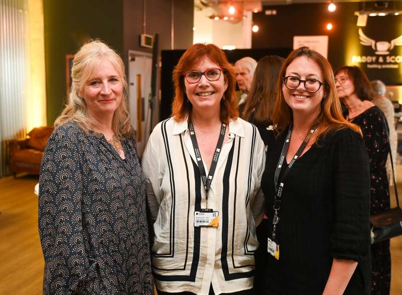 Three individuals standing together and smiling at a social event, wearing lanyards with name tags.