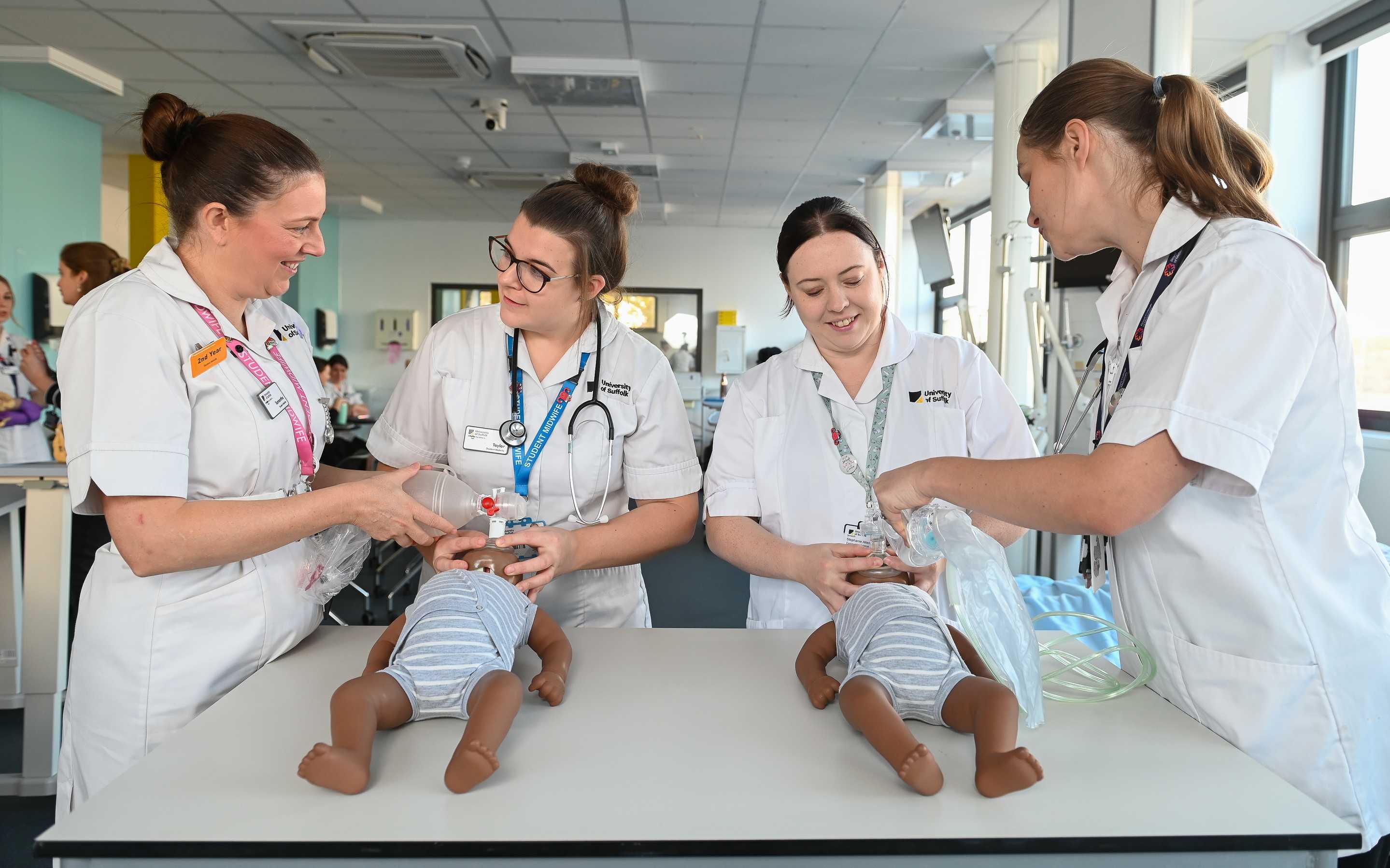 Four midwifery students in white uniforms with two baby dolls