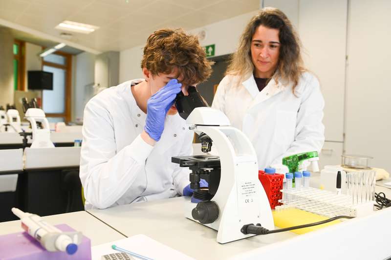 A student looking through a microscope with lecturer