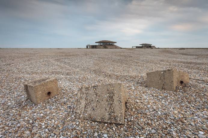 The landscape at Orford Ness. One of the pagodas is visible in the background, with shingle beach and some rocks visible in the foreground. Photo credit: Justin Minns/National Trust