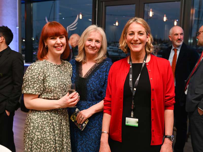 Three people smiling at a social event, with one holding a glass of sparkling wine.