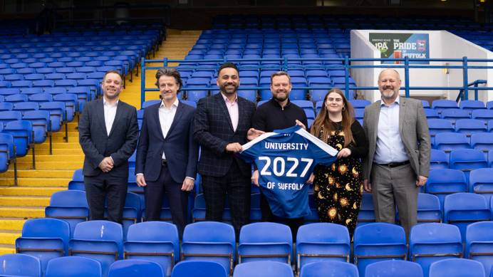 A photo from partners at the University of Suffolk and Ipswich Town Football Club standing holding a football shirt in one of the stands